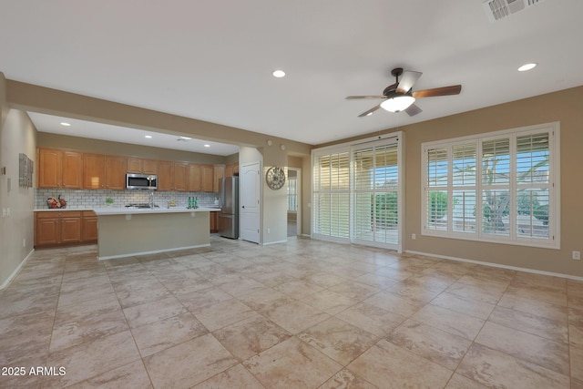 kitchen featuring ceiling fan, appliances with stainless steel finishes, tasteful backsplash, and an island with sink