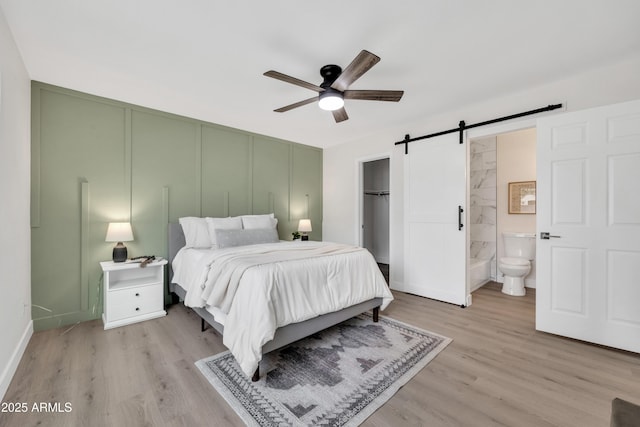 bedroom with light wood-type flooring, a closet, ensuite bath, and a barn door