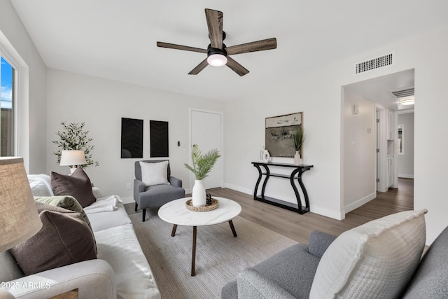 living area with baseboards, wood finished floors, visible vents, and a ceiling fan