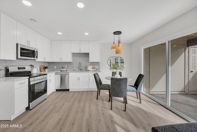 kitchen with tasteful backsplash, visible vents, stainless steel appliances, light wood-type flooring, and a sink