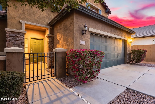 exterior space featuring a garage, concrete driveway, stone siding, fence, and stucco siding