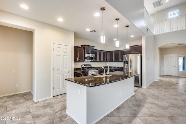 kitchen featuring arched walkways, visible vents, dark stone counters, stainless steel appliances, and a sink