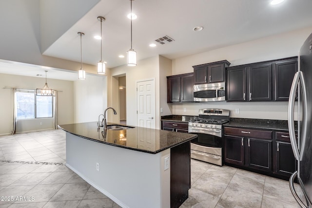 kitchen featuring sink, hanging light fixtures, dark stone counters, stainless steel appliances, and a kitchen island with sink