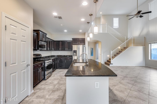 kitchen with arched walkways, stainless steel appliances, a sink, visible vents, and dark stone countertops