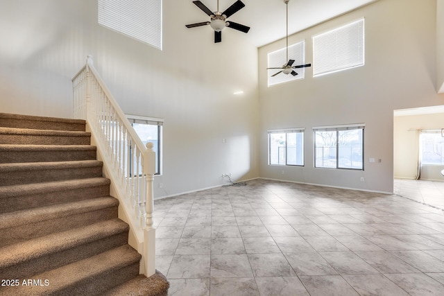 unfurnished living room with baseboards, stairway, a ceiling fan, and a healthy amount of sunlight