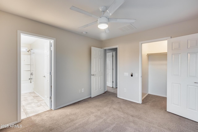 unfurnished bedroom with ensuite bath, ceiling fan, a walk in closet, light colored carpet, and a closet