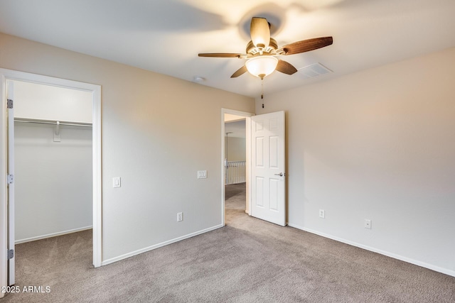 unfurnished bedroom with a walk in closet, light colored carpet, ceiling fan, and a closet