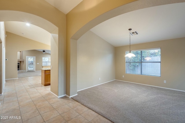 carpeted spare room with lofted ceiling, a tiled fireplace, and ceiling fan