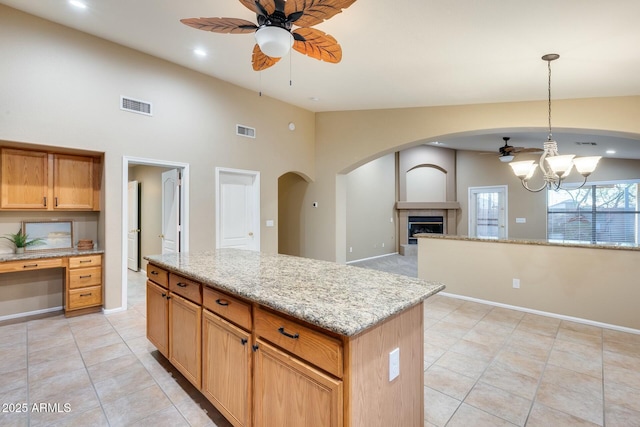 kitchen with light stone counters, decorative light fixtures, ceiling fan with notable chandelier, and a kitchen island