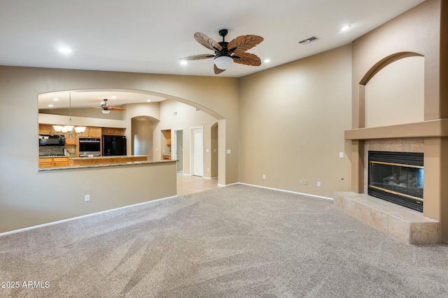 unfurnished living room featuring vaulted ceiling, a fireplace, ceiling fan with notable chandelier, and light carpet