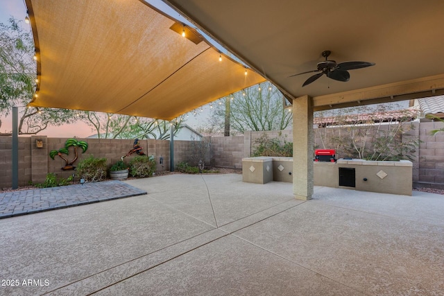 patio terrace at dusk with ceiling fan and exterior kitchen