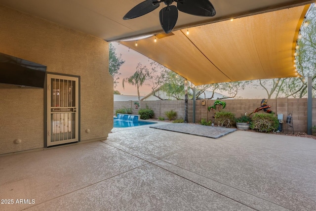 patio terrace at dusk with ceiling fan and a fenced in pool