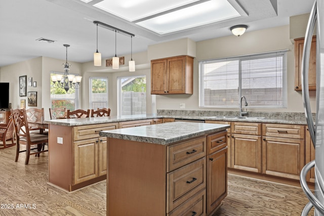kitchen with a sink, a peninsula, light wood-type flooring, a kitchen island, and visible vents