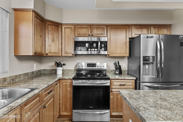 kitchen with light countertops, appliances with stainless steel finishes, brown cabinetry, and a sink