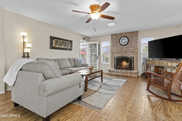 living area with ceiling fan, a wealth of natural light, wood finished floors, and a fireplace