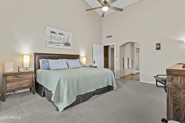 carpeted bedroom featuring a ceiling fan, a towering ceiling, visible vents, arched walkways, and baseboards