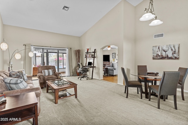 carpeted living area featuring high vaulted ceiling, baseboards, arched walkways, and visible vents