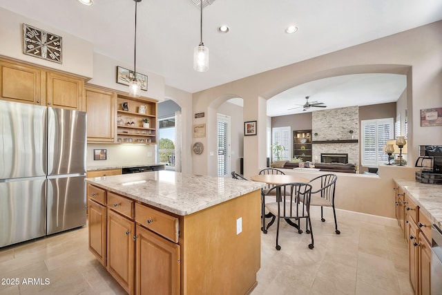 kitchen featuring a kitchen island, light stone counters, freestanding refrigerator, arched walkways, and open shelves