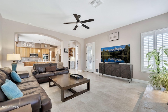 living room featuring ceiling fan, arched walkways, visible vents, and baseboards