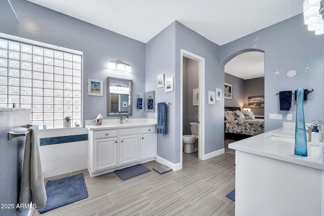 ensuite bathroom featuring vanity, toilet, baseboards, and ensuite bathroom