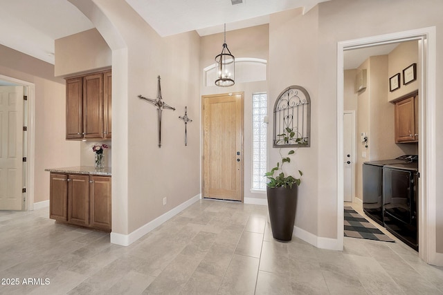 entrance foyer with baseboards, an inviting chandelier, a high ceiling, separate washer and dryer, and arched walkways