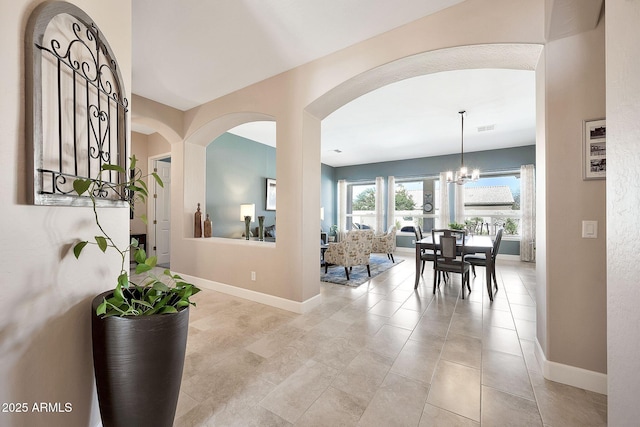 hallway with light tile patterned floors, visible vents, baseboards, and a notable chandelier