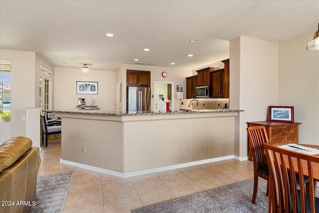 kitchen featuring light stone counters, light tile patterned floors, kitchen peninsula, appliances with stainless steel finishes, and decorative backsplash