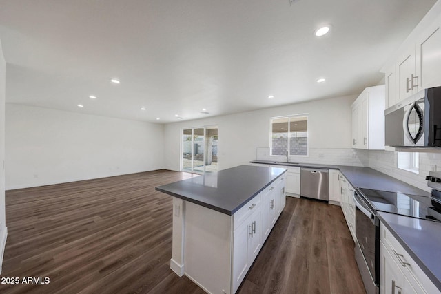 kitchen with stainless steel appliances, dark wood-type flooring, white cabinetry, tasteful backsplash, and dark countertops