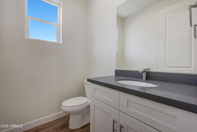 half bath featuring toilet, vanity, baseboards, and wood finished floors