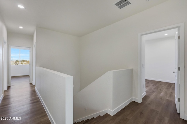 hall with dark wood-style floors, baseboards, visible vents, and an upstairs landing