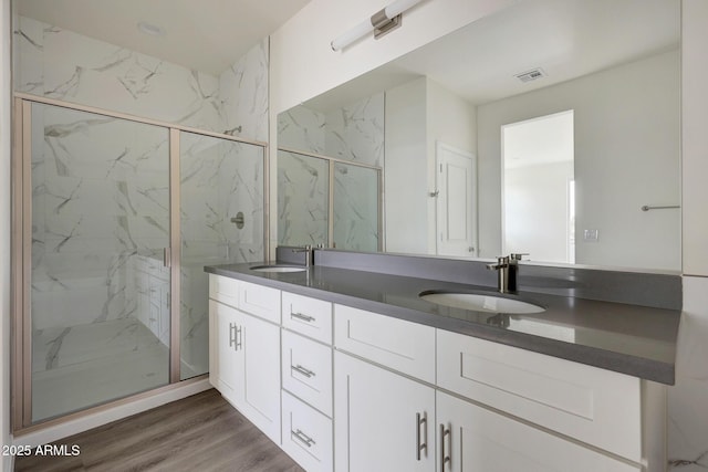 bathroom with double vanity, a marble finish shower, a sink, and wood finished floors