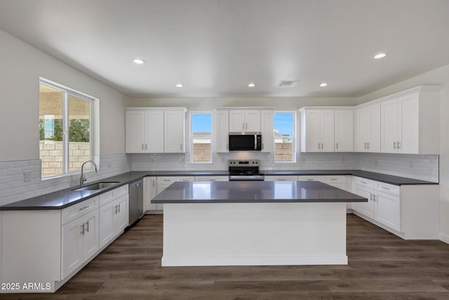 kitchen featuring appliances with stainless steel finishes, dark countertops, a kitchen island, and white cabinetry