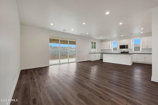 unfurnished living room featuring baseboards, dark wood finished floors, and a healthy amount of sunlight