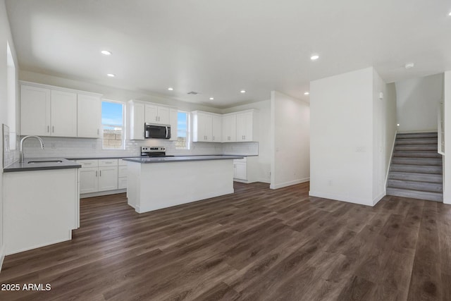 kitchen with stainless steel appliances, dark countertops, a sink, and white cabinetry