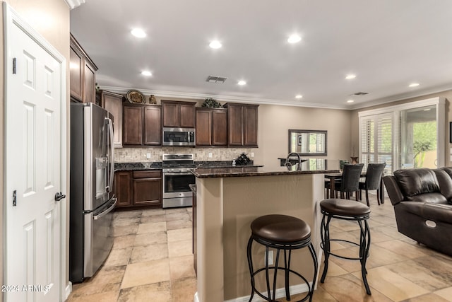 kitchen with a center island with sink, ornamental molding, appliances with stainless steel finishes, and tasteful backsplash