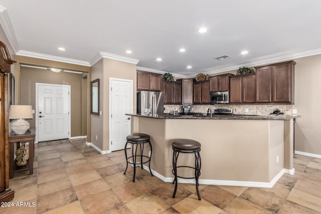 kitchen featuring backsplash, crown molding, a kitchen bar, a center island with sink, and appliances with stainless steel finishes