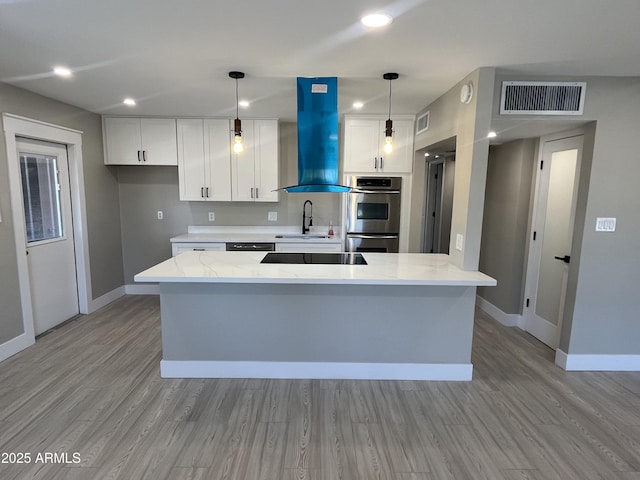 kitchen featuring visible vents, double oven, island range hood, white cabinets, and a sink