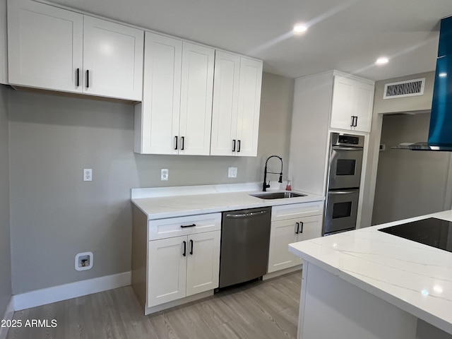 kitchen with white cabinets, a sink, light wood finished floors, stainless steel appliances, and baseboards