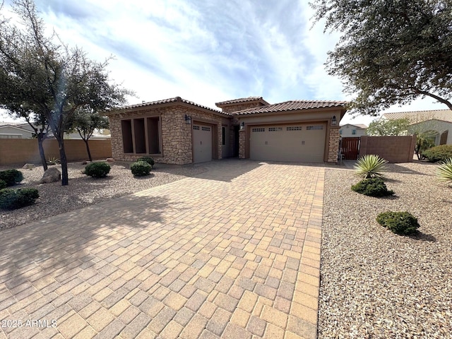 view of front of house featuring fence, an attached garage, stone siding, a tile roof, and decorative driveway