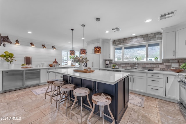 kitchen with a kitchen island, a kitchen bar, white cabinetry, sink, and hanging light fixtures