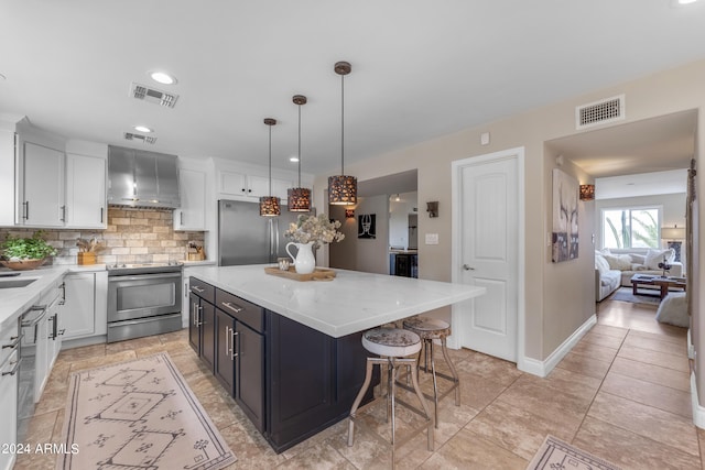 kitchen with white cabinetry, stainless steel appliances, pendant lighting, wall chimney exhaust hood, and a center island