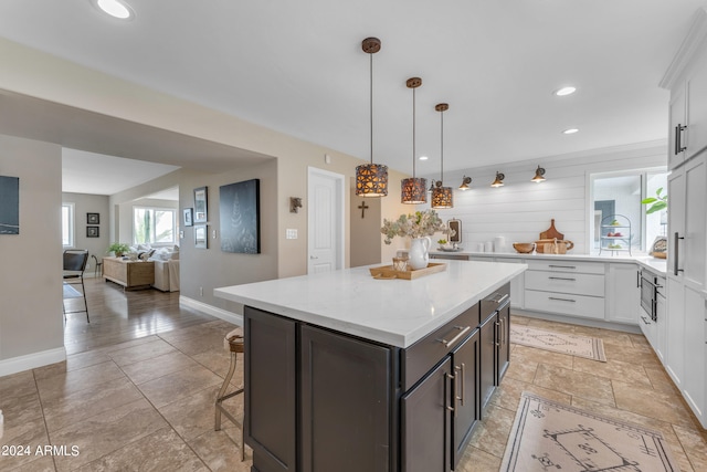 kitchen with a kitchen breakfast bar, built in microwave, hanging light fixtures, a kitchen island, and white cabinets