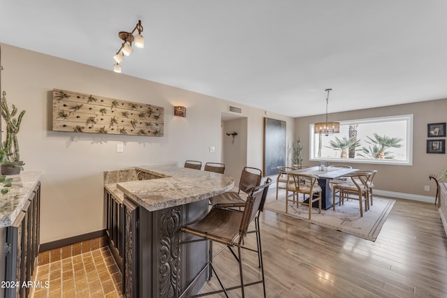 kitchen with an inviting chandelier, kitchen peninsula, wood-type flooring, light stone countertops, and a breakfast bar