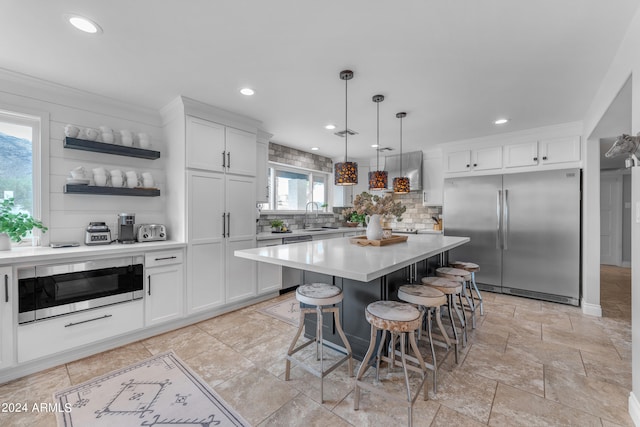 kitchen featuring decorative light fixtures, built in appliances, a kitchen island, white cabinets, and a breakfast bar