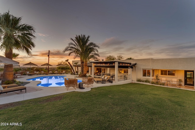 pool at dusk featuring a patio area, outdoor lounge area, and a yard