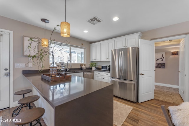 kitchen featuring kitchen peninsula, stainless steel appliances, pendant lighting, white cabinets, and sink