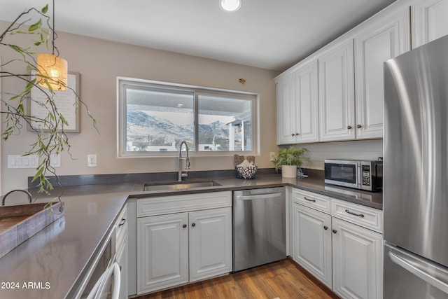 kitchen with appliances with stainless steel finishes, white cabinets, pendant lighting, light hardwood / wood-style flooring, and sink