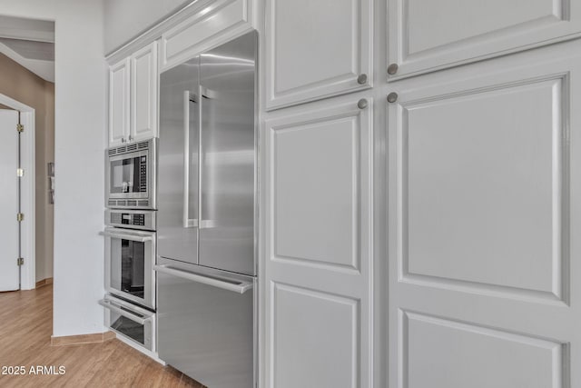 kitchen with white cabinetry, built in appliances, and light hardwood / wood-style flooring