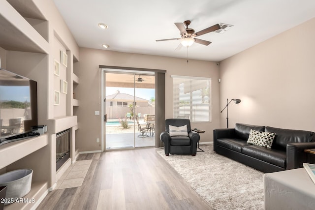1333 W Deer Creek Rd, Phoenix, AZ 85045 - living area featuring a fireplace with flush hearth, baseboards, ceiling fan, and light wood finished floors