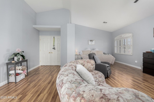 bedroom with wood finished floors, visible vents, baseboards, vaulted ceiling, and a closet